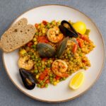brown rice seafood paella with clams, mussels, shrimp, corn, peas, and Calabrian chili garnish