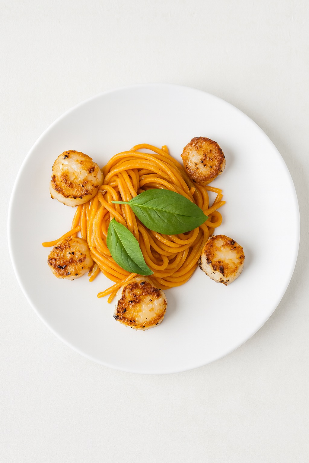 Whole wheat spaghetti in cherry tomato sauce topped with seared scallops and basil